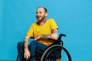 un hombre en un silla de ruedas sonrisa mira a el cámara en un camiseta con tatuajes en su brazos se sienta en un azul estudio fondo, un lleno vida, un real persona foto
