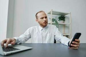 A man in a wheelchair a businessman in the office works at a laptop and holds a phone in his hands, thoughtfulness, integration into society, the concept of working a person with disabilities photo