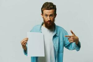 Portrait of an adult male on a gray background with a white sheet of paper in his hands for your design and text, layout, copy space, space for text, finger pointing photo