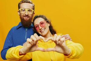 Man and woman couple smiling cheerfully and crooked with glasses, on yellow background, symbols signs and hand gestures, family shoot, newlyweds. photo
