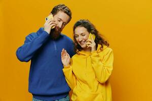 Woman and man cheerful couple with phones in hand talking on cell phone crooked smile cheerful, on yellow background. The concept of real family relationships, talking on the phone, work online. photo