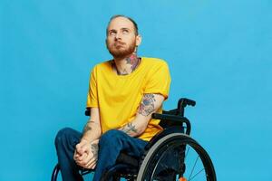 a man sits in a wheelchair in a t-shirt on a blue background in the studio, the concept of a free barrier-free environment for people with disabilities photo