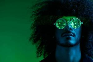 Fashion portrait of a man with curly hair on a green background with sunglasses, multinational, colored pink light, trendy, modern concept. photo