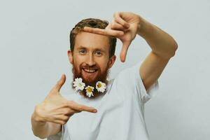 Portrait of a funny man in a white T-shirt with flowers daisies in his beard on a white isolated background, copy place. Holiday concept and congratulations. photo