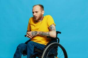 un hombre se sienta en un silla de ruedas en un camiseta en un azul antecedentes en el estudio, el concepto de un gratis sin barreras ambiente para personas con discapacidades foto