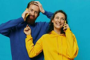 mujer y hombre alegre Pareja con Los telefonos en su manos torcido sonrisa alegre, en azul antecedentes. el concepto de real familia relaciones, hablando en el teléfono, trabajo en línea. foto