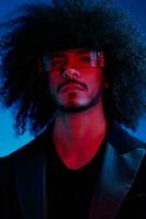 Fashion portrait of a man with curly hair on a blue background wearing red sunglasses, multinational, colored light, trendy, modern concept. photo