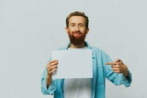 retrato de un adulto masculino en un gris antecedentes con un blanco sábana de papel en su manos para tu diseño y texto, disposición, Copiar espacio, espacio para texto, dedo señalando foto