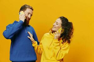 Woman and man cheerful couple with phones in hand talking on cell phone crooked smile cheerful, on yellow background. The concept of real family relationships, talking on the phone, work online. photo