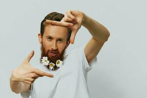 Portrait of a funny man in a white T-shirt with flowers daisies in his beard on a white isolated background, copy place. Holiday concept and congratulations. photo