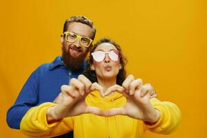 hombre y mujer Pareja sonriente alegremente y torcido con anteojos, en amarillo fondo, símbolos señales y mano gestos, familia disparar, recién casados. foto