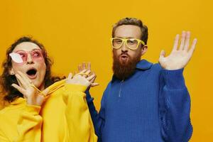 Man and woman couple smiling cheerfully and crooked with glasses, on yellow background, symbols signs and hand gestures, family shoot, newlyweds. photo