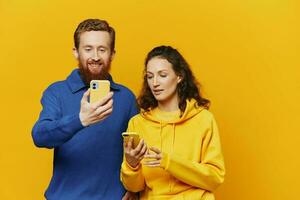 Man and woman couple smiling merrily with phone in hand social media viewing photos and videos, on yellow background, symbols signs and hand gestures, family freelancers.