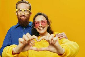 hombre y mujer Pareja sonriente alegremente y torcido con anteojos, en amarillo fondo, símbolos señales y mano gestos, familia disparar, recién casados. foto