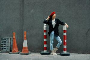 Fashion woman standing leaning against a wall street against a background of the city road works tourist in stylish clothes with red lips and red beret, travel, cinematic color, retro vintage style. photo