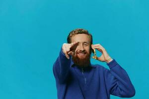 Portrait of a man with a phone in his hands does looking at it and talking on the phone, on a blue background. Communicating online social media, lifestyle photo