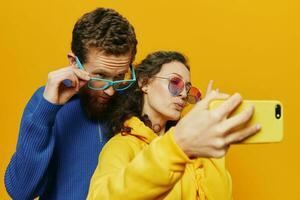 Woman and man funny couple with phones hand social networking and communication crooked do selfies smile fun, on yellow background. The concept of real family relationships, freelancers, work online. photo