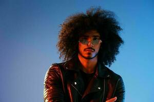 Portrait of a stylish man with curly hair on a blue background multinational, colored light, trendy glasses, modern concept. photo