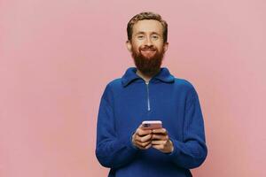 Portrait of a man with a phone in his hands doing looking at it and talking on the phone, on a pink background. Communicating online social media, lifestyle photo