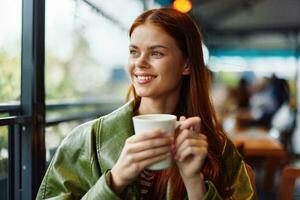 Portrait of a woman influencer drinking a drink from a mug in a cafe and smiling with her teeth looking out the window, content blogger close-up photo