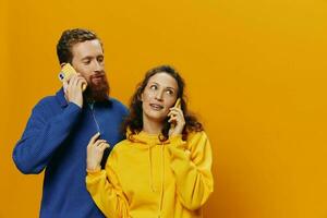 Man and woman couple smiling merrily with phone in hand social media viewing photos and videos, on yellow background, symbols signs and hand gestures, family freelancers.