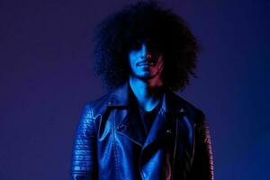 Portrait of fashion man with curly hair on blue background multinational, colored light, black leather jacket trend, modern concept. photo