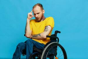 un hombre se sienta en un silla de ruedas consideración en un camiseta en un azul antecedentes en el estudio, el concepto de un gratis sin barreras ambiente para personas con discapacidades foto