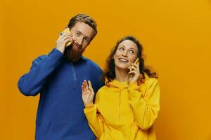 Woman and man cheerful couple with phones in hand talking on cell phone crooked smile cheerful, on yellow background. The concept of real family relationships, talking on the phone, work online. photo