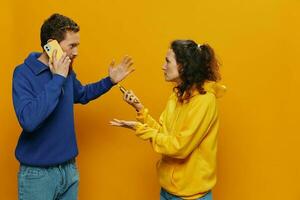 mujer hombre alegre Pareja con Los telefonos en mano social redes y comunicación torcido sonrisa divertido y luchar, en amarillo antecedentes. el concepto de real familia relaciones, autónomos, trabajo en línea. foto