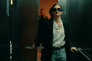 elegante mujer en negro chaqueta y Gafas de sol posando en ascensor, Moda modelo, oscuro cinematográfico ligero y color, glamour Clásico foto