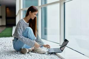 A woman smiling with teeth sits with a laptop by the large windows of a building in the city talking via video link through a computer, the concept of work and leisure in the big city photo