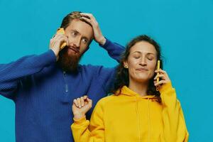 mujer y hombre alegre Pareja con Los telefonos en su manos torcido sonrisa alegre, en azul antecedentes. el concepto de real familia relaciones, hablando en el teléfono, trabajo en línea. foto