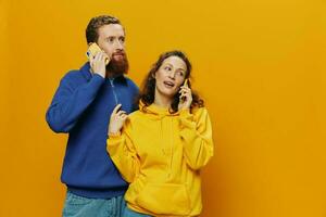 Man and woman couple smiling merrily with phone in hand social media viewing photos and videos, on yellow background, symbols signs and hand gestures, family freelancers.
