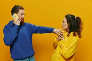 mujer hombre alegre Pareja con Los telefonos en mano social redes y comunicación torcido sonrisa divertido y luchar, en amarillo antecedentes. el concepto de real familia relaciones, autónomos, trabajo en línea. foto