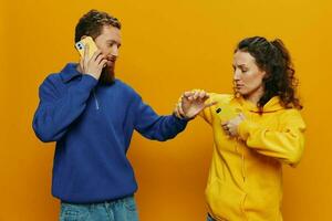 Woman man cheerful couple with phones in hand social networking and communication crooked smile fun and fight, in yellow background. The concept of real family relationships, freelancers, work online. photo