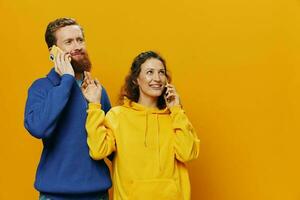 Woman and man cheerful couple with phones in hand talking on cell phone crooked smile cheerful, on yellow background. The concept of real family relationships, talking on the phone, work online. photo