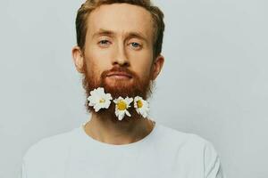 Portrait of a funny man in a white T-shirt with flowers daisies in his beard on a white isolated background, copy place. Holiday concept and congratulations. photo