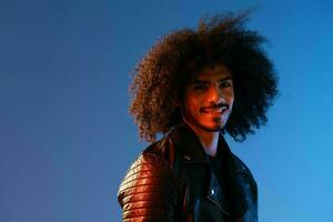 Portrait of a stylish man with curly hair on a blue background multinational, colored light, black leather jacket trend, modern concept. photo