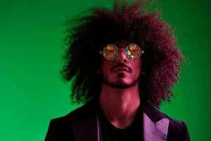 Fashion portrait of a man with curly hair on a green background with sunglasses, multinational, colored pink light, trendy, modern concept. photo