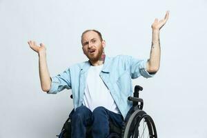 A man in a wheelchair and pointing a finger at, copy space, with tattoos on his hands sits on a gray studio background, health concept a person with disabilities, a real person photo