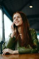 Woman with red hair freelance blogger sitting in a cafe talking on the phone and smiling, hipster girl in trendy clothes lifestyle photo