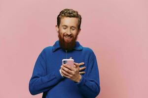Portrait of a man with a phone in his hands doing looking at it and talking on the phone, on a pink background. Communicating online social media, lifestyle photo