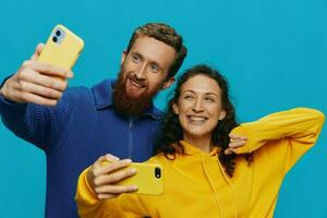 Woman and man funny couple with phones in hand taking selfies crooked smile fun, on blue background. The concept of real family relationships, talking on the phone, work online. photo