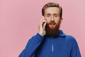 Portrait of a man with a phone in his hands doing looking at it and talking on the phone, on a pink background. Communicating online social media, lifestyle photo