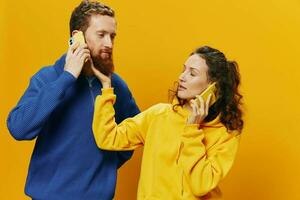 mujer y hombre alegre Pareja con Los telefonos en mano hablando en célula teléfono torcido sonrisa alegre, en amarillo antecedentes. el concepto de real familia relaciones, hablando en el teléfono, trabajo en línea. foto