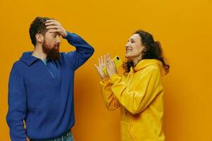 mujer hombre alegre Pareja con Los telefonos en mano social redes y comunicación torcido sonrisa divertido y luchar, en amarillo antecedentes. el concepto de real familia relaciones, autónomos, trabajo en línea. foto