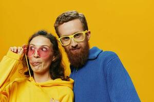 Man and woman couple smiling cheerfully and crooked with glasses, on yellow background, symbols signs and hand gestures, family shoot, newlyweds. photo