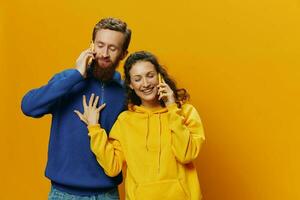 Woman and man cheerful couple with phones in hand talking on cell phone crooked smile cheerful, on yellow background. The concept of real family relationships, talking on the phone, work online. photo
