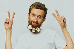 Portrait of a funny man in a white T-shirt with flowers daisies in his beard on a white isolated background, copy place. Holiday concept and congratulations. photo