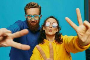 un mujer y un hombre divertido Pareja arrancando y demostración señales con su manos sonriente alegremente, en un azul fondo, el concepto de un real relación en un familia. foto